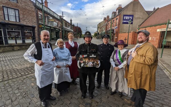 Costumed members of Beamish Museum staff standing on The 1900s Town street with a box of Beamish Cluedo